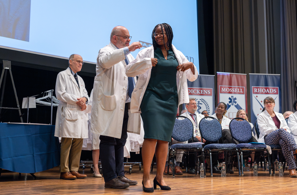 A faculty member helps a student don a white coat at the White Coat ceremony.